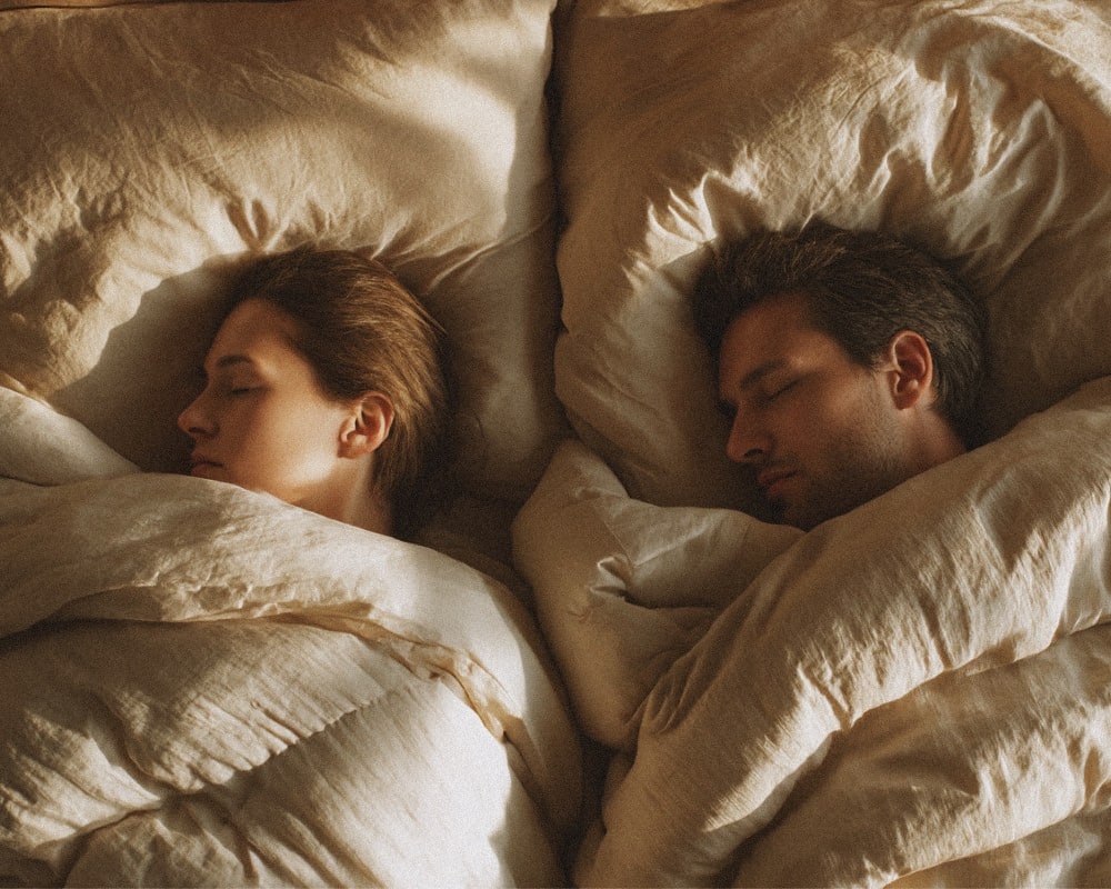 Couple dans sa chambre avec deux couettes une personne dans les bras